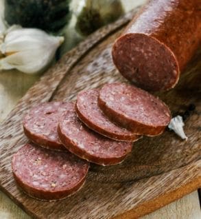 A wooden cutting board with several slices of sausage.