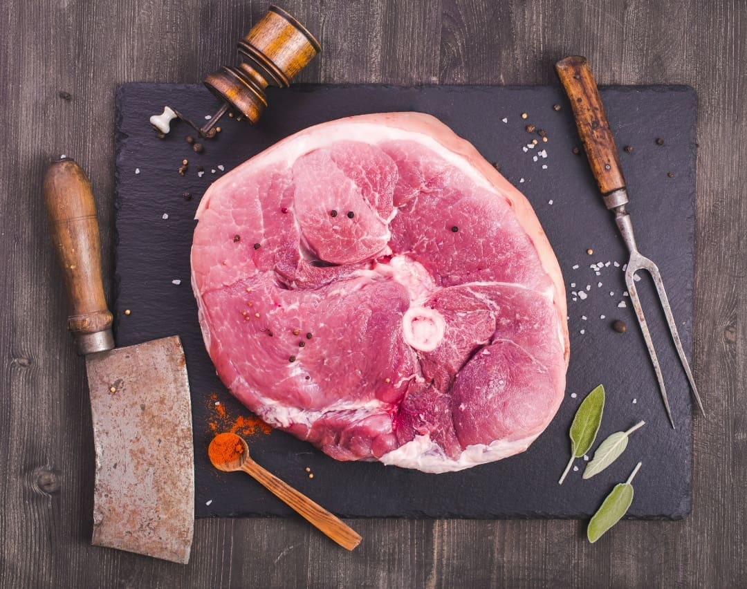 A raw meat on a cutting board with knives and spatulas.